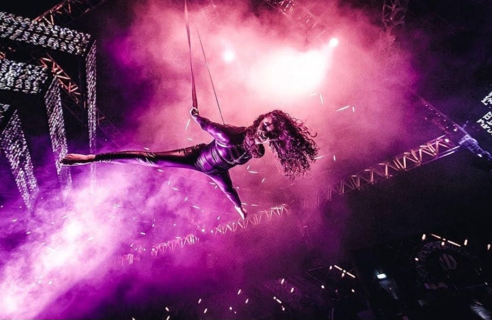 Aerial performer flying above a concert stage in magenta light